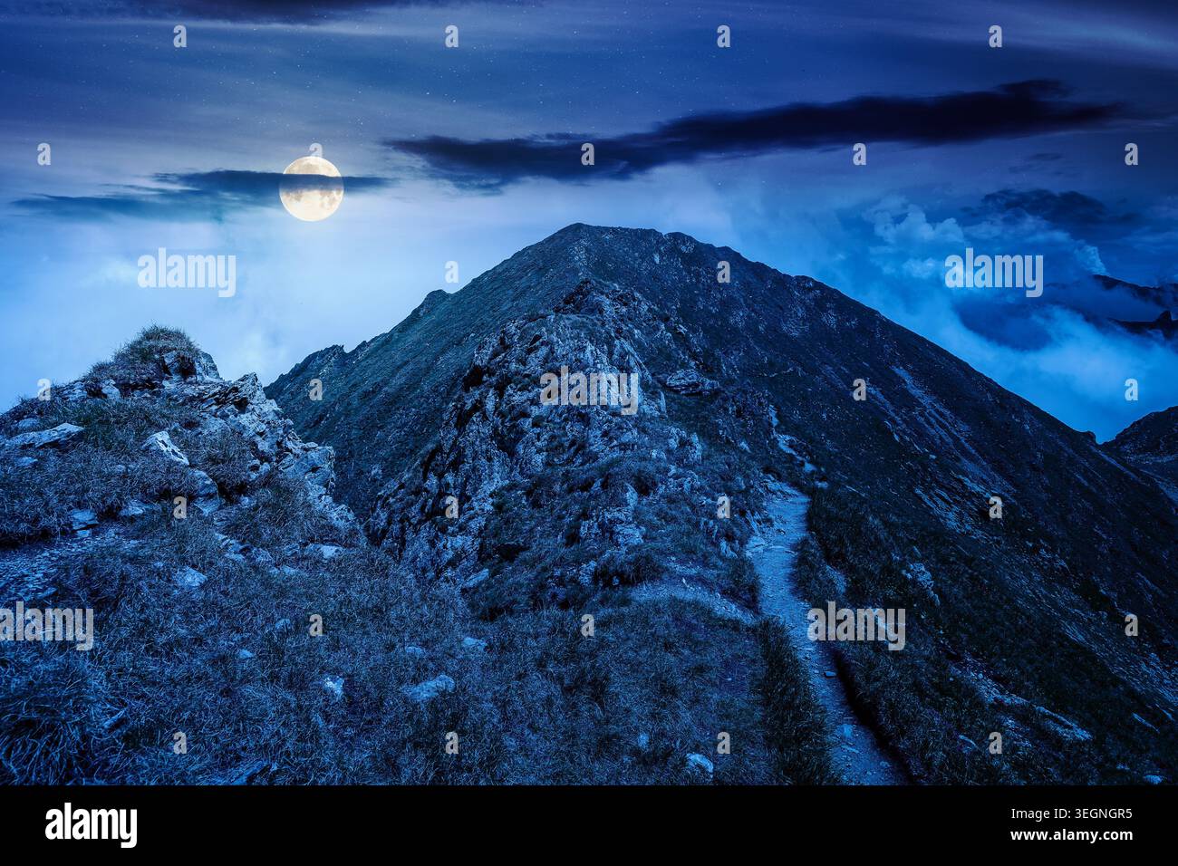 mountain scenery in summer at night. gorgeous mountainous landscape. background with rocky cliffs and grassy hillsides under a cloudy sky. full moon o Stock Photo