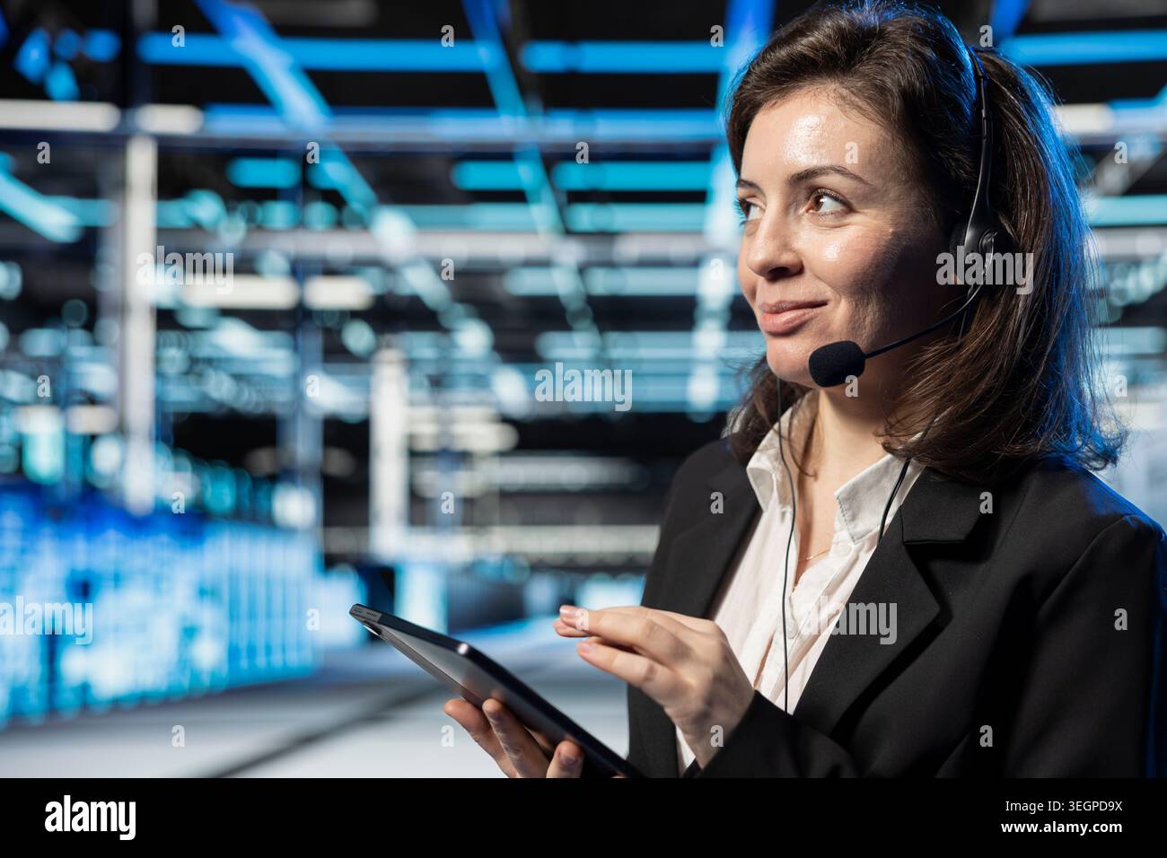 Friendly data center customer service agent uses headset mic to talk with users. Smiling server room employee talking in microphone during remote call, resolving support tickets for enterprise clients Stock Photo