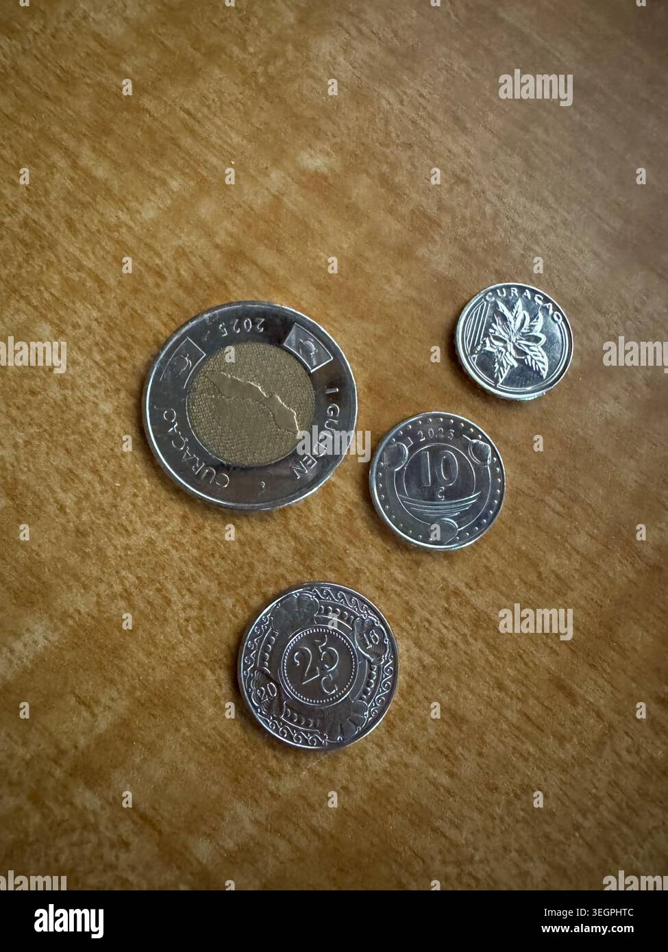 Close-up overhead shot of four different Netherlands Antilles golden coins, including a Curacao coin, resting on a textured wooden surface. - Smartphone Captured Stock Image