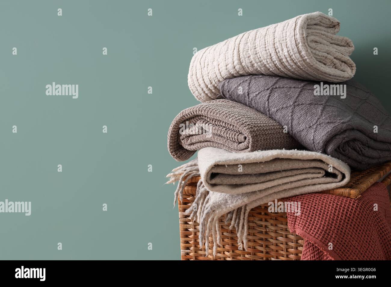 Wicker basket with stack of different cozy blankets on turquoise background Stock Photo