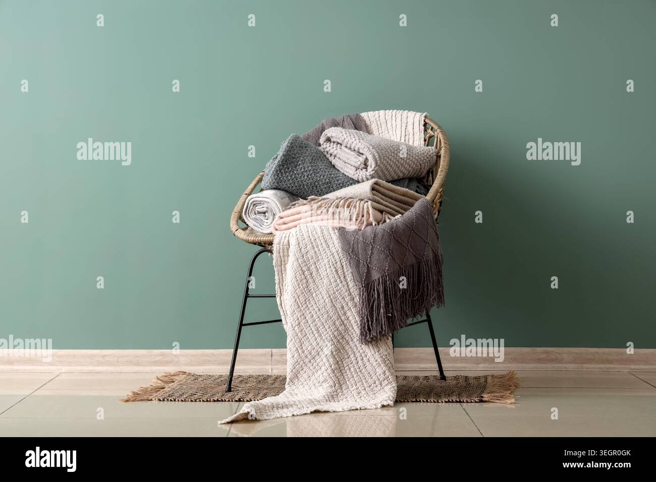 Wicker chair with different cozy blankets near turquoise wall in room Stock Photo