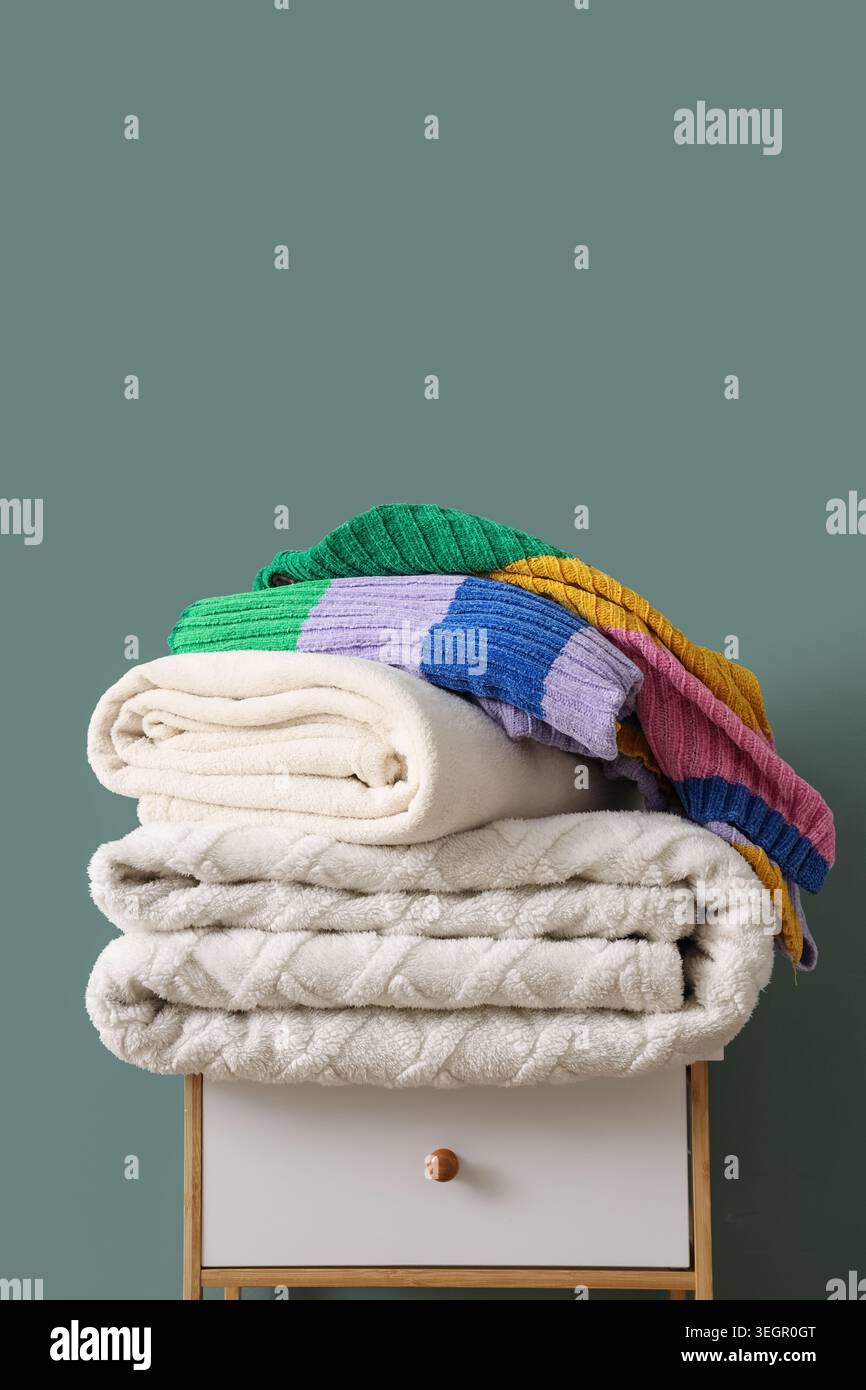 Stack of different cozy blankets on bedside table against turquoise background Stock Photo