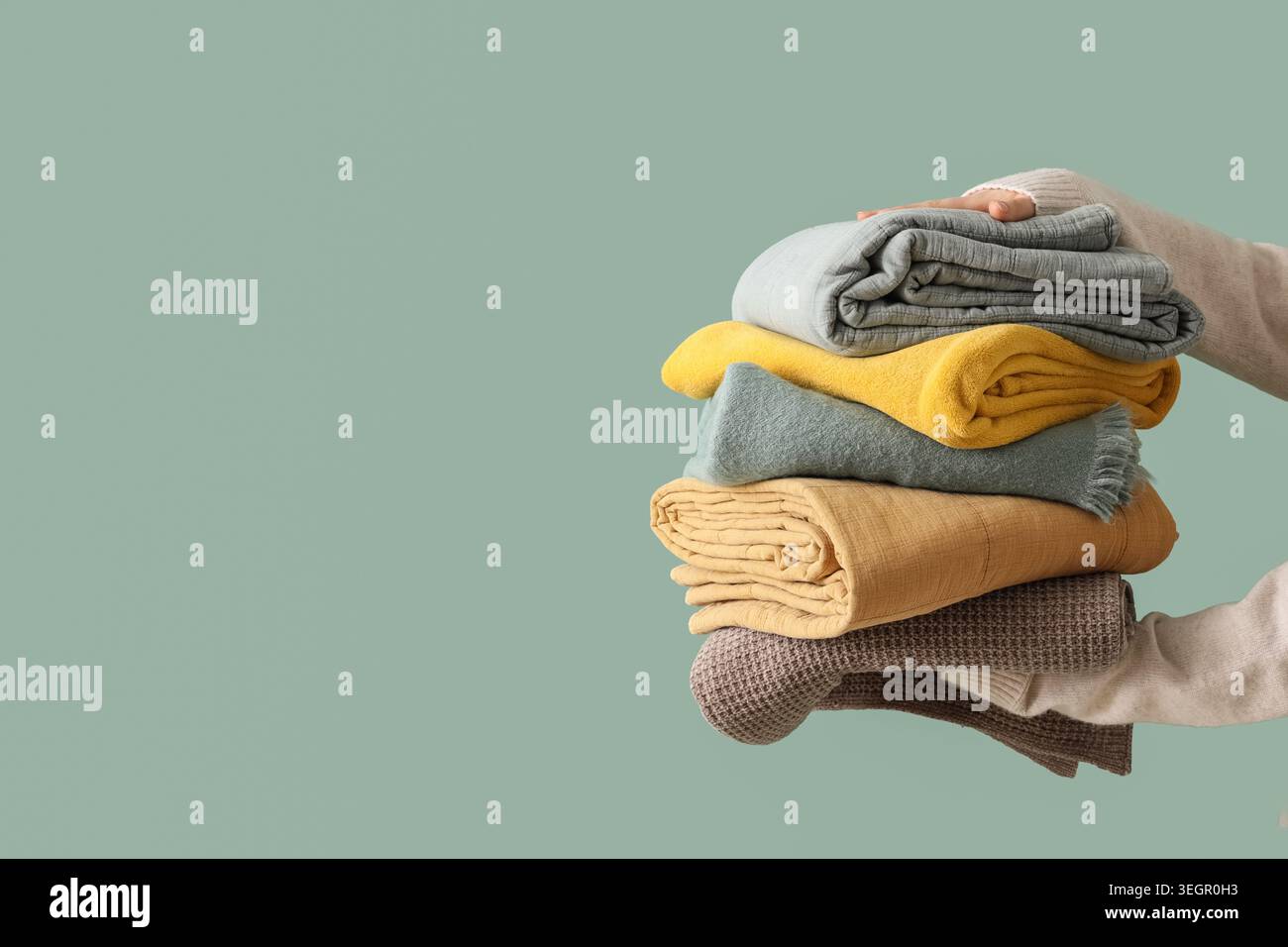 Female hands with stack of different blankets on turquoise background Stock Photo