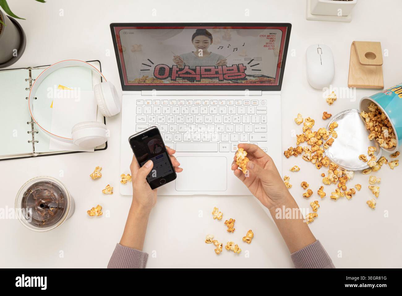 A person sits at a desk, working on a laptop, surrounded by popcorn, while watching a video on the screen. Stock Photo