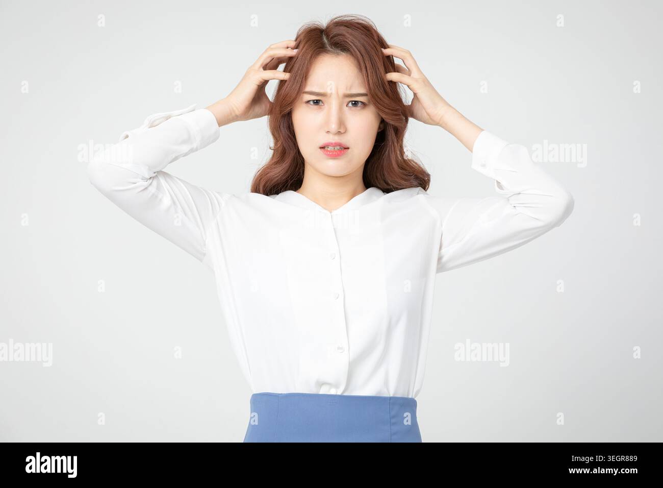 A young woman with a worried expression, holding her temples and looking off to the side. Stock Photo