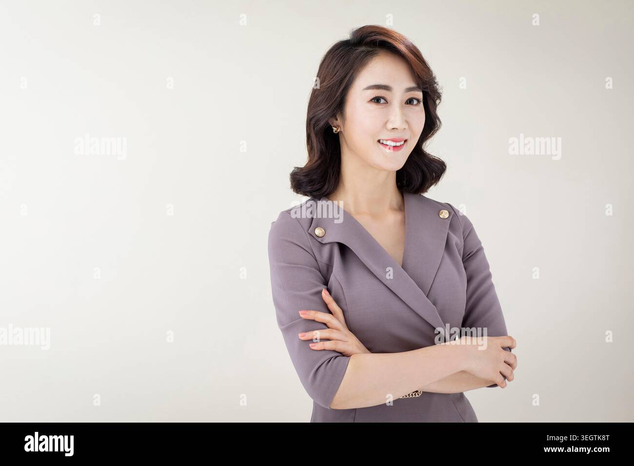 A woman in a business suit stands confidently with her arms crossed, smiling slightly as she looks to the side. Stock Photo