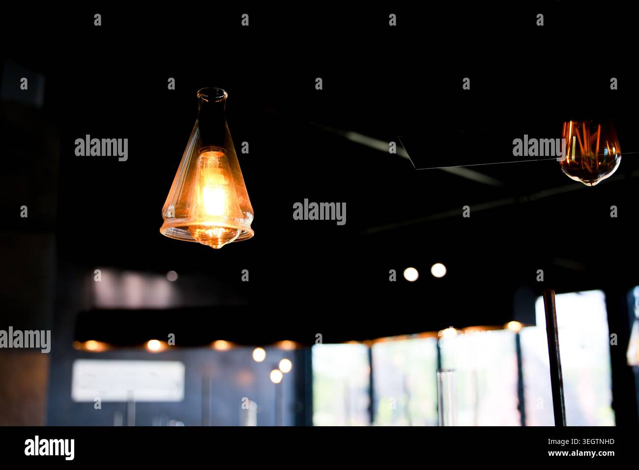 Vintage glass pendant light bulb glowing warm yellow illuminating dark interior room creating cozy atmospheric mood with blurred background Stock Photo