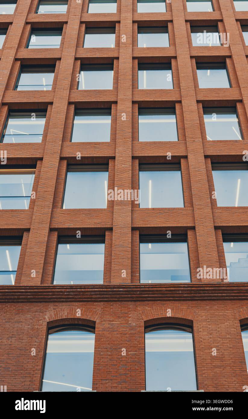 Rising view of a contemporary brick building featuring a grid of many square windows and arched windows on a lower level Stock Photo