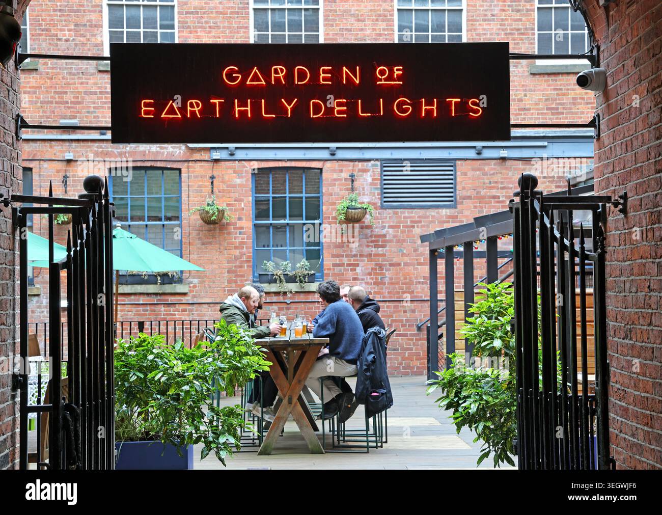Customers relax beneath the Garden of Earthly Delights red neon sign in the courtyard at Nation of Shopkeepers pub in Leeds, West Yorkshire. Stock Photo