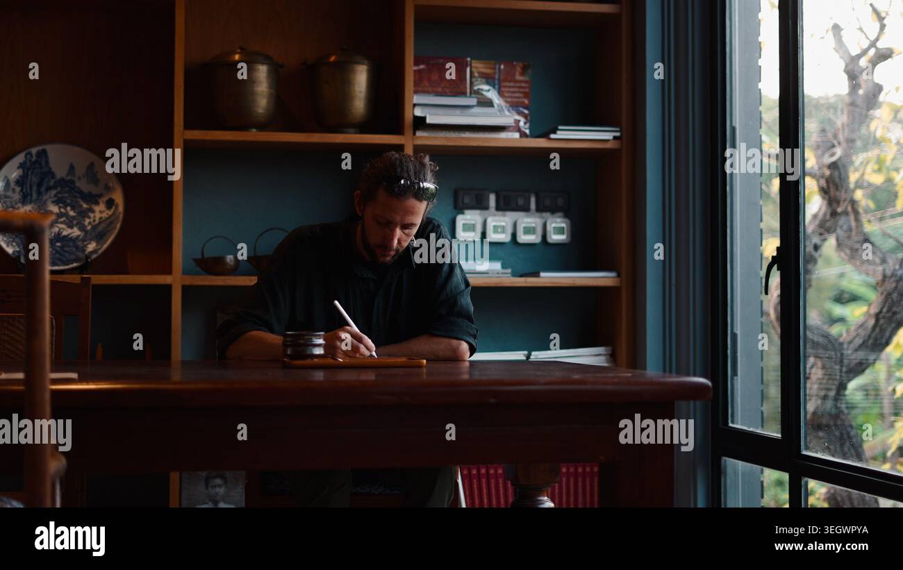 Man writing on tablet at study desk in a traditional home environment ...