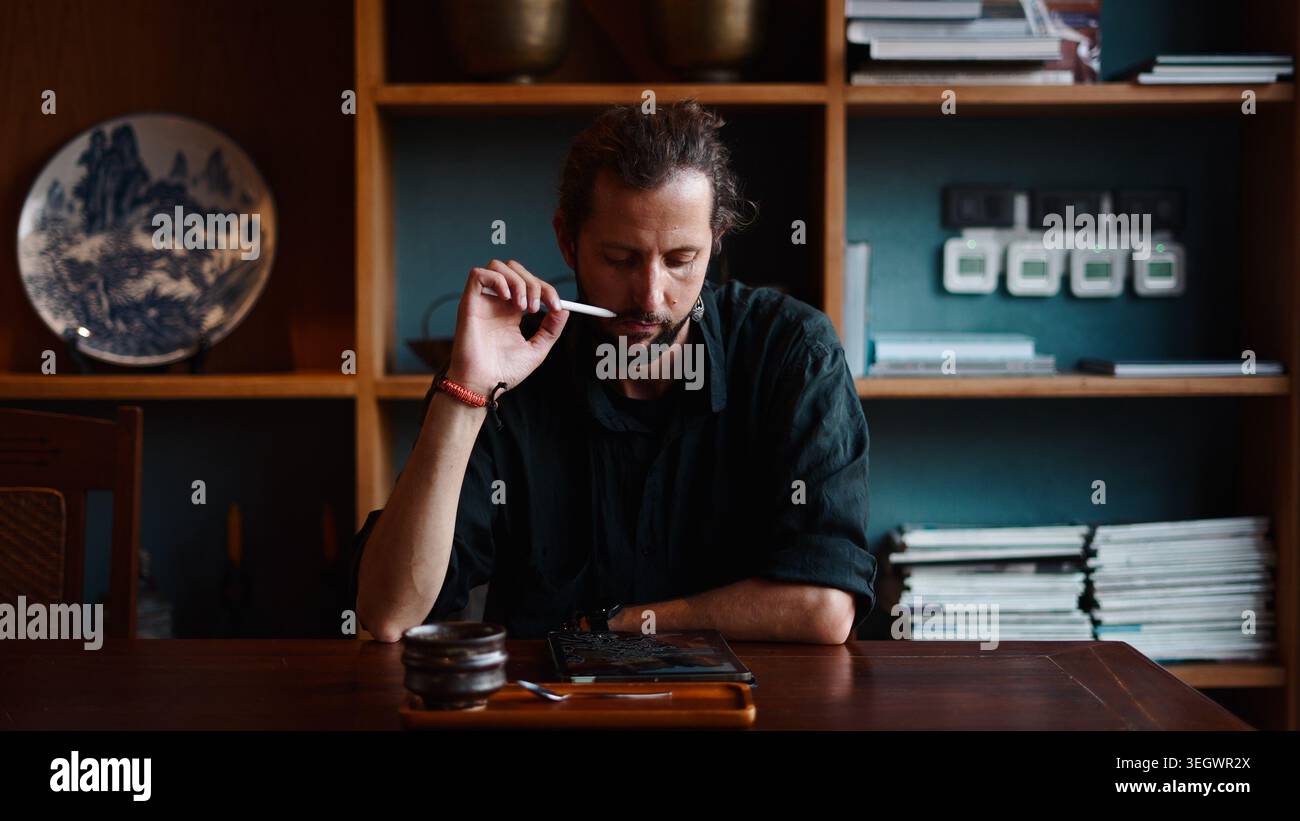 Creative designer analyzing digital artwork on a tablet, deeply concentrating at work Stock Photo
