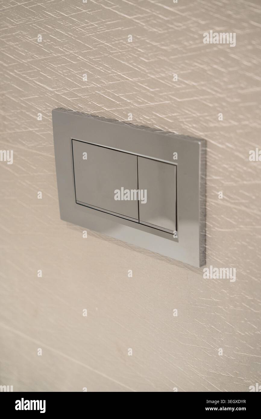 Chrome dual flush plate with two rectangular buttons mounted on a light textured wall, providing a sleek, modern, and water-efficient solution for Stock Photo