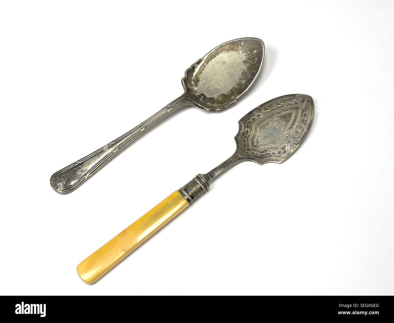 Two tarnished engraved antique silver spoons utensils including a server with a yellow handle and a spoon isolated on white background - Smartphone Captured Stock Image