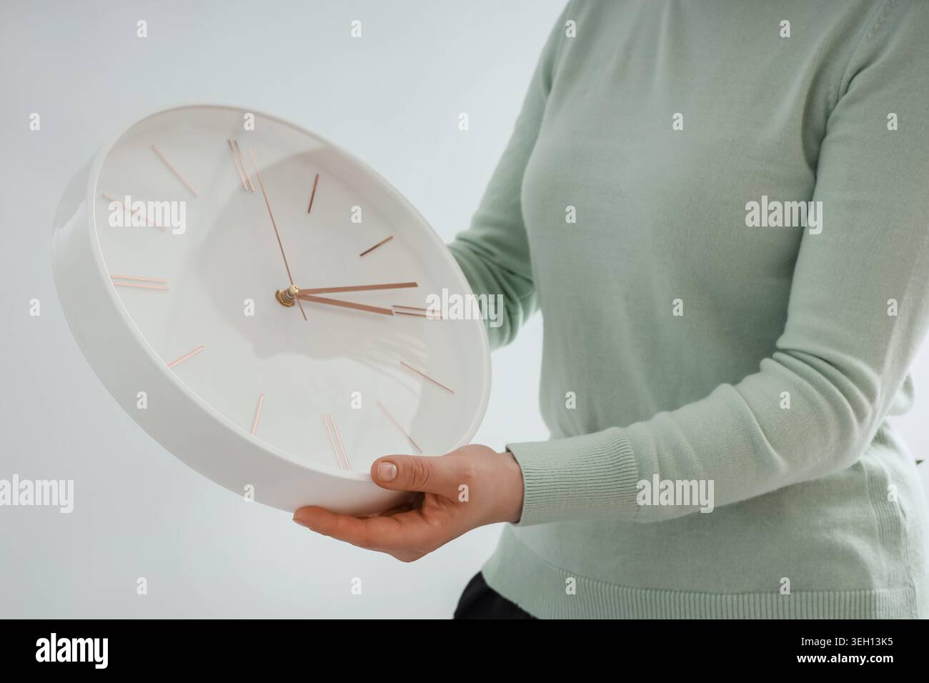 Woman setting time on wall clock on light background. Daylight saving time concept Stock Photo