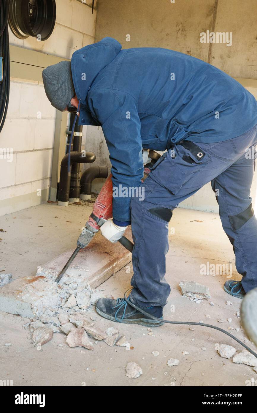Worker using jackhammer to break concrete floor indoors Stock Photo