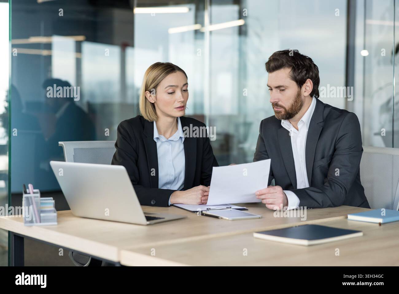 Two diverse business professionals collaborating during a meeting, discussing important documents and working together on a project in a modern office environment Stock Photo