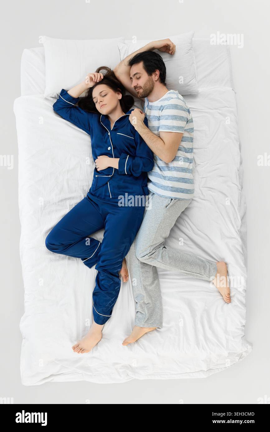 Daughter making funny face while parents laugh on bright white bedding. Stock Photo