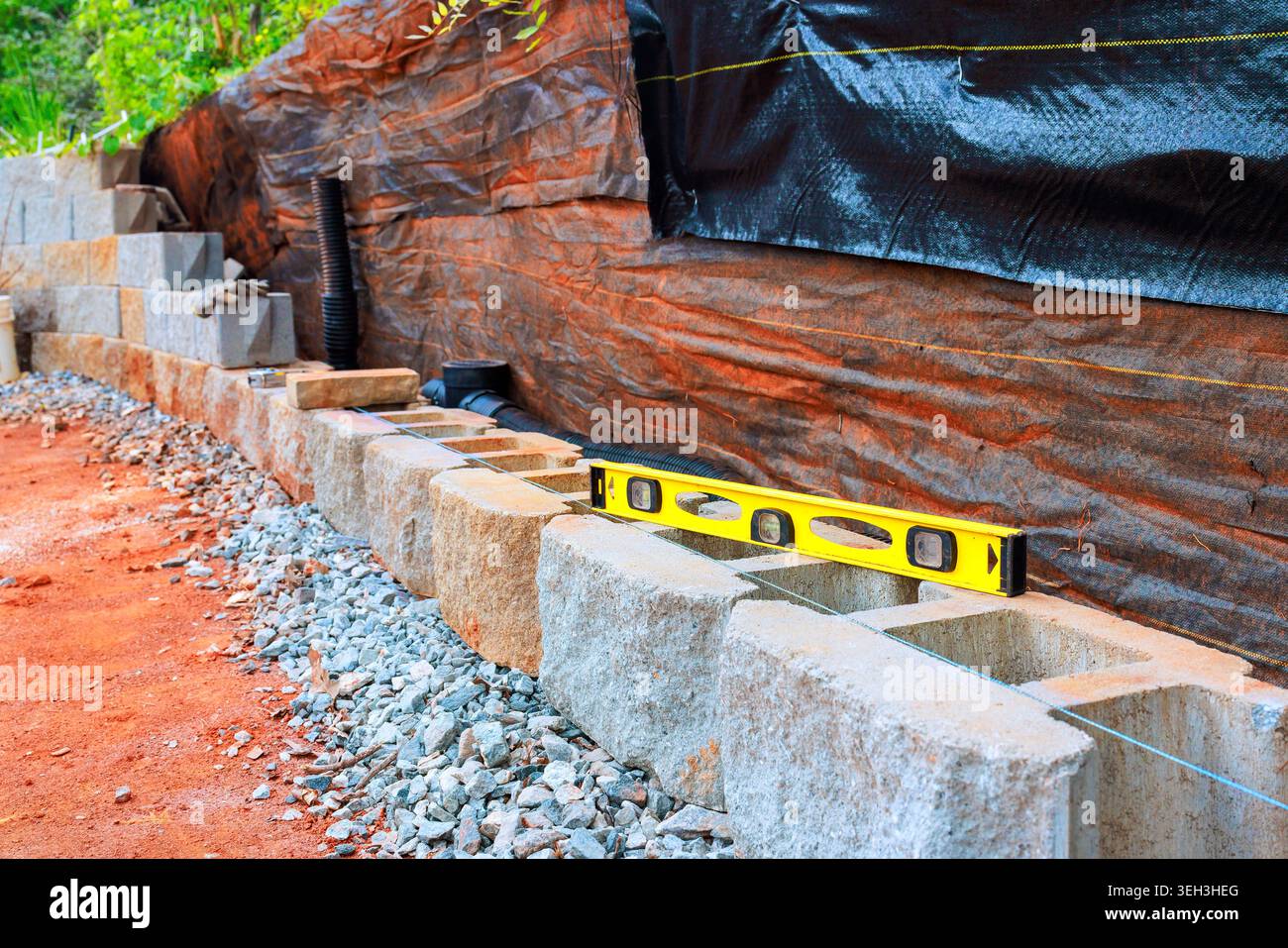 Workers are building retaining stone wall using concrete blocks checking level of structure with tool. Stock Photo