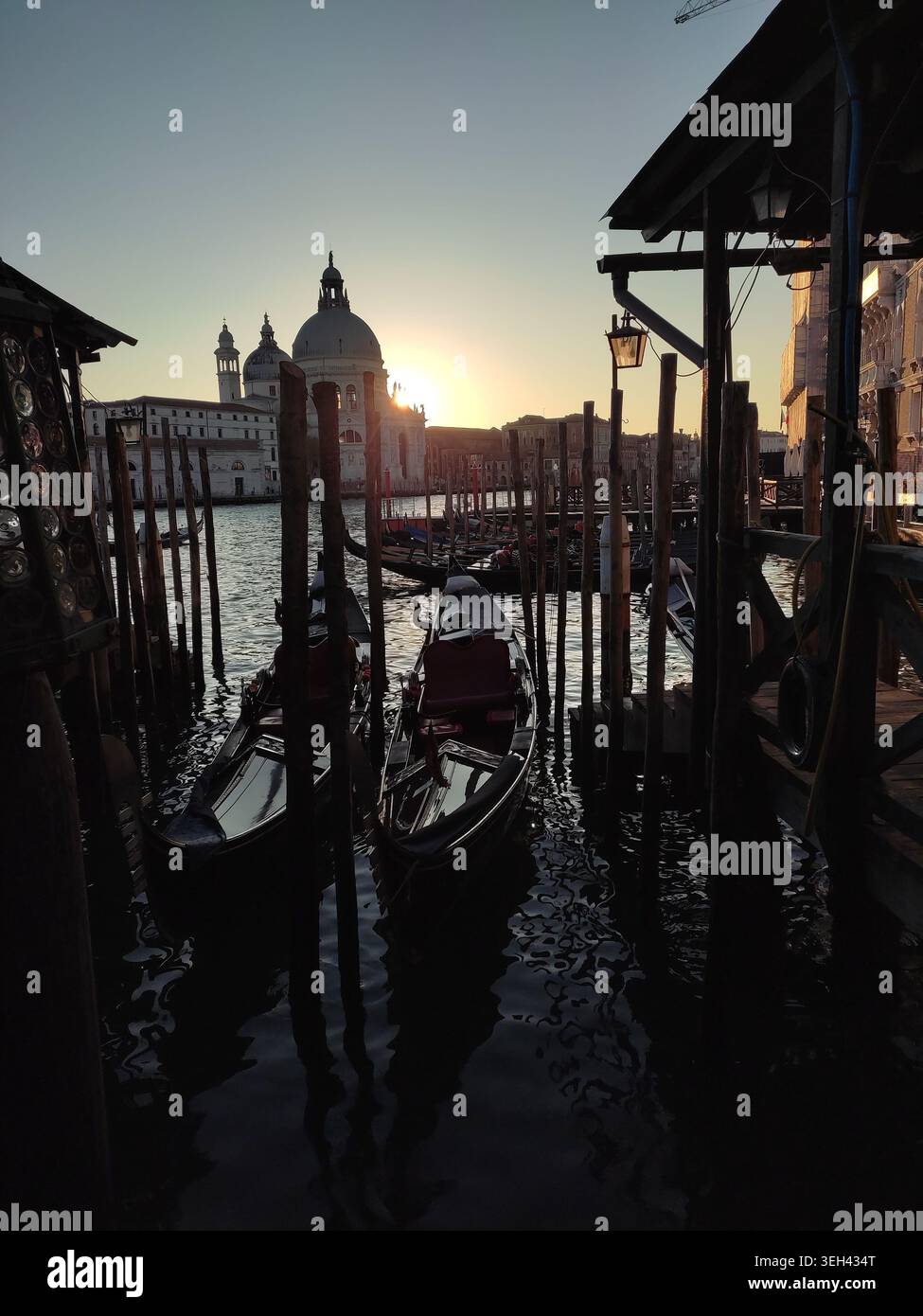Gondolas resting on calm waters as the sun sets over Venice, capturing ...
