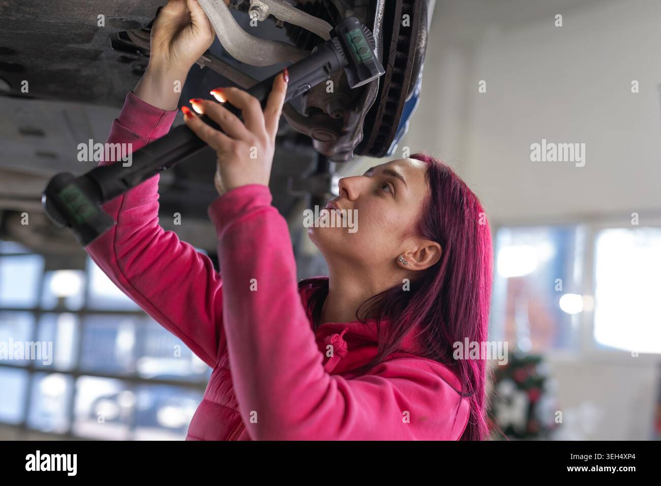 Female car mechanic inspects and repairs a vehicle in a busy garage. She uses tools and diagnostic equipment for maintenance work. Stock Photo
