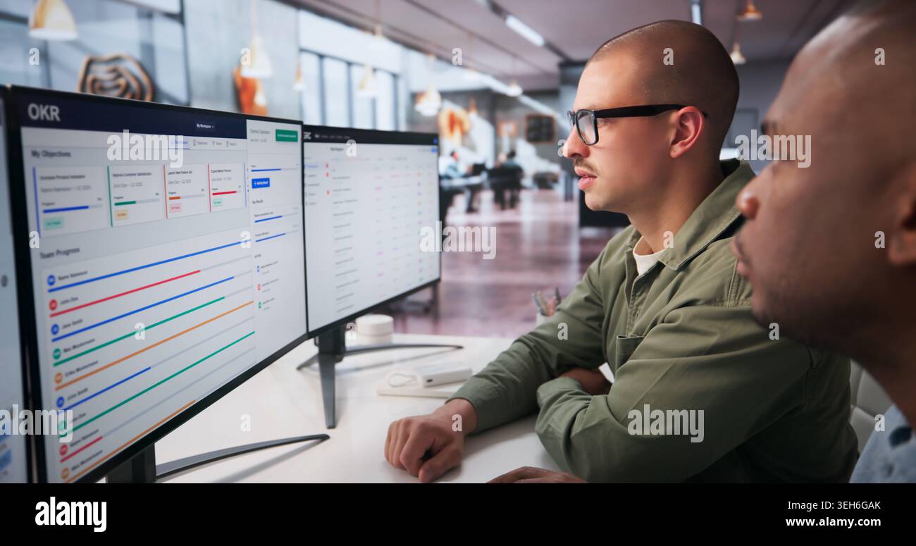 Two Young Professionals Collaborate On Business Goals Using Software Dashboard. Stock Photo