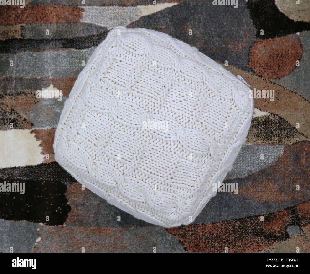 Square woolen white pouf on multicolored carpet background. Top view. Stock Photo