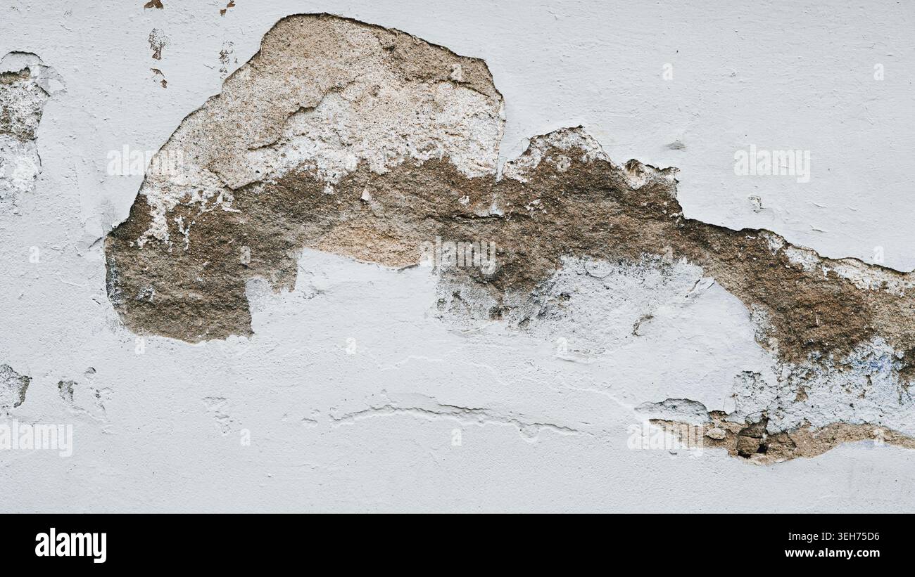 A close up shot of a weathered concrete wall where the grey paint is peeling away to reveal the rough. Stock Photo