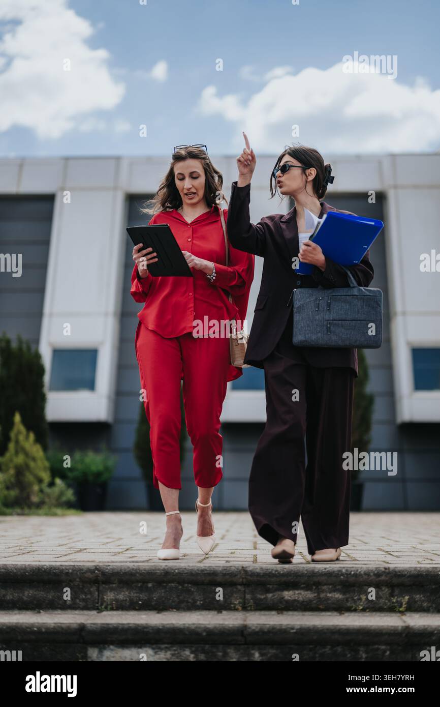 Two professional women walking and discussing documents outside an office building Stock Photo