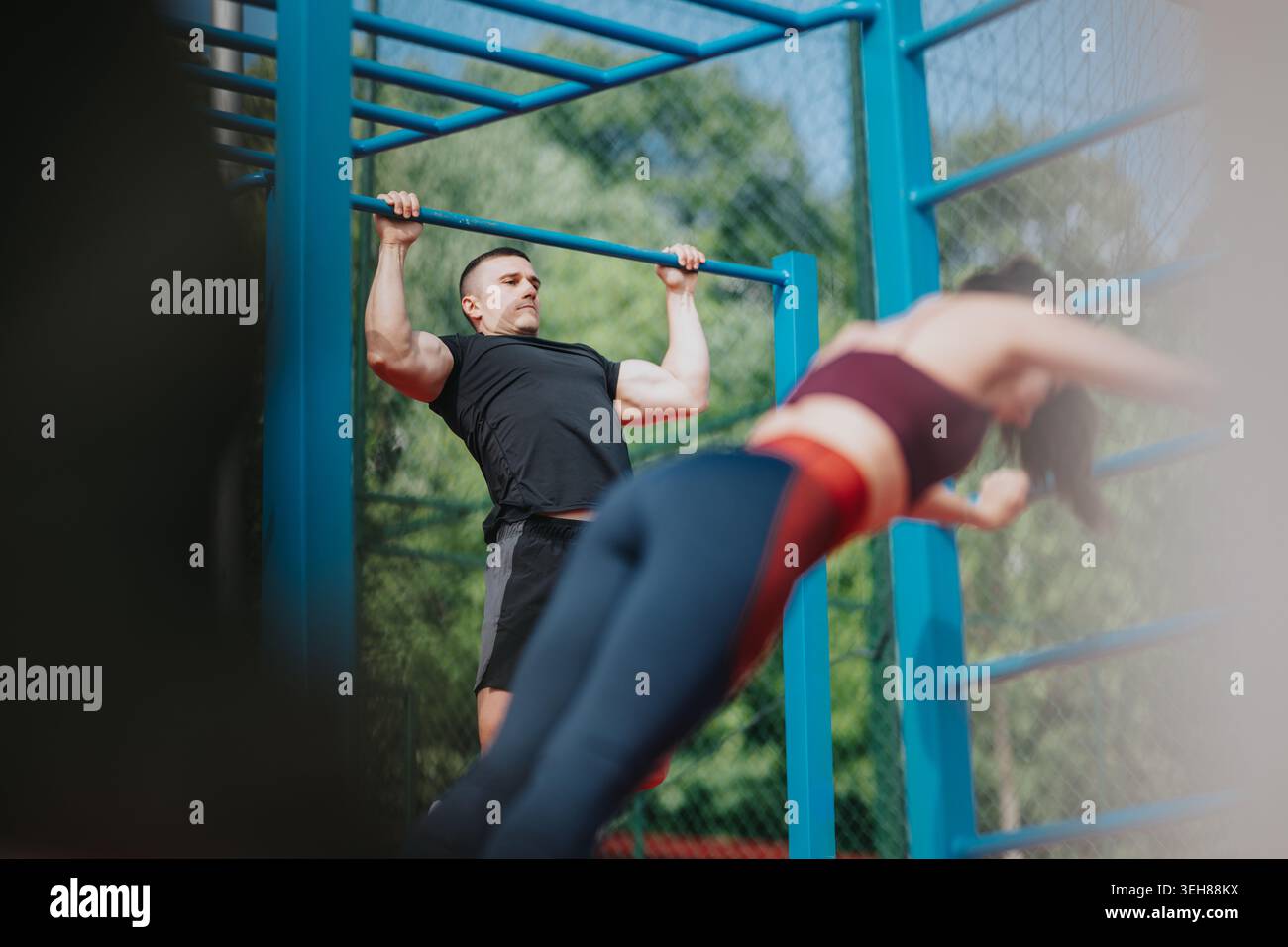 Man doing pull-up at outdoor gym while partner works on parallel bars in athletic workout Stock Photo