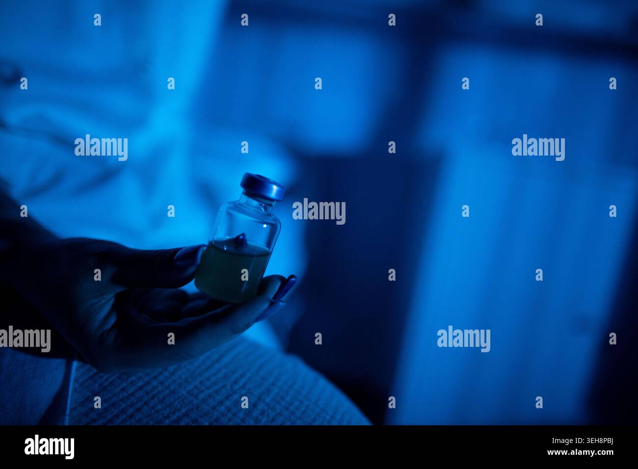 Hand pouring pills from bottle onto bedsheet, blue lowlight closeup of fingers and wrist, textured fabric, mood of insomnia and latenight fatigue, sin Stock Photo