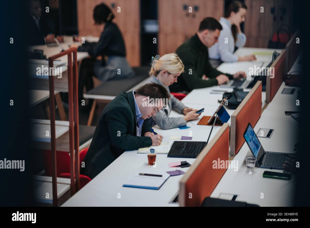 Business professionals working together in a modern co-working space taking notes and using laptops Stock Photo