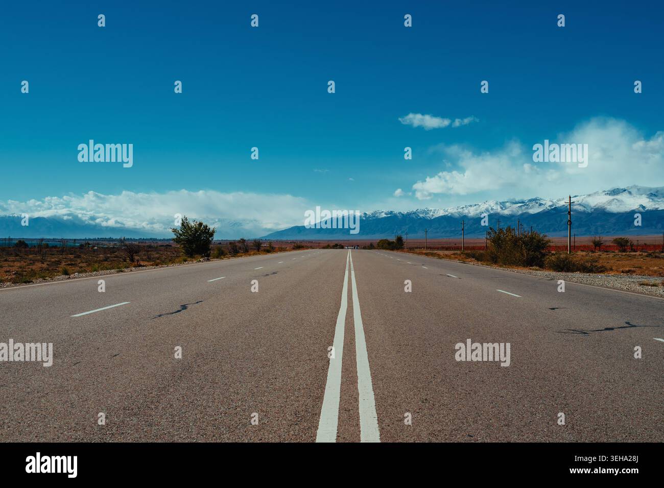 Lonely road with double solid line on sunny day with mountains Stock Photo