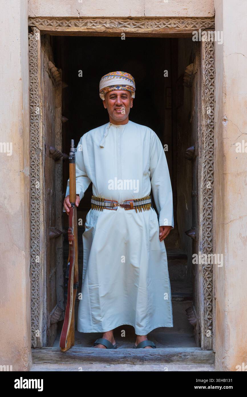 An armed guard in traditional Omani attire with turban (massar) a long ...