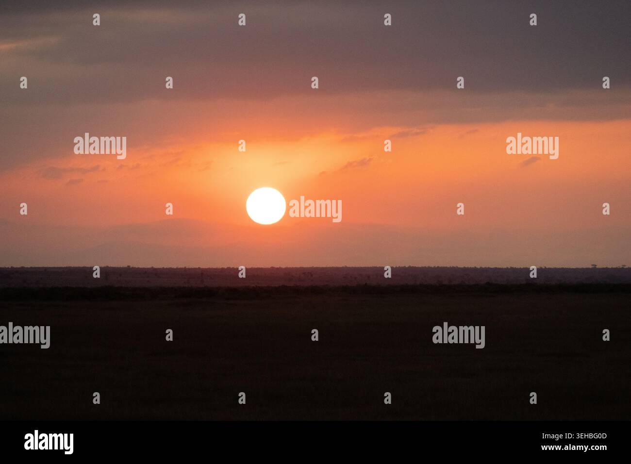 Bright orange sun rising over the flat horizon of the savanna in Amboseli National Park Kenya Stock Photo
