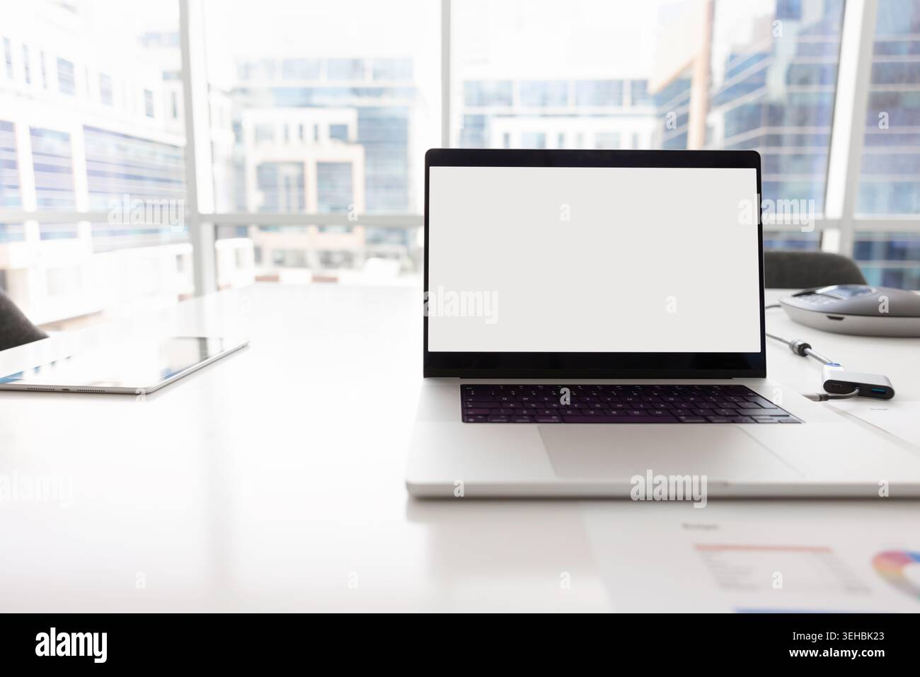 Papers with charts next to laptop with white mockup screen Stock Photo