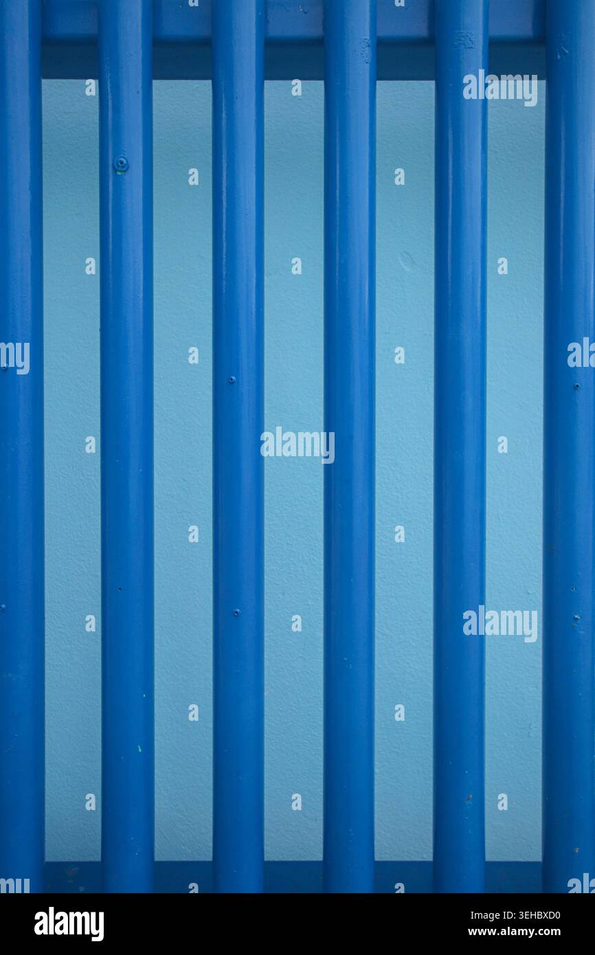 Vertical blue metal bars fence creating a modern geometric pattern background texture in an urban industrial environment. Stock Photo