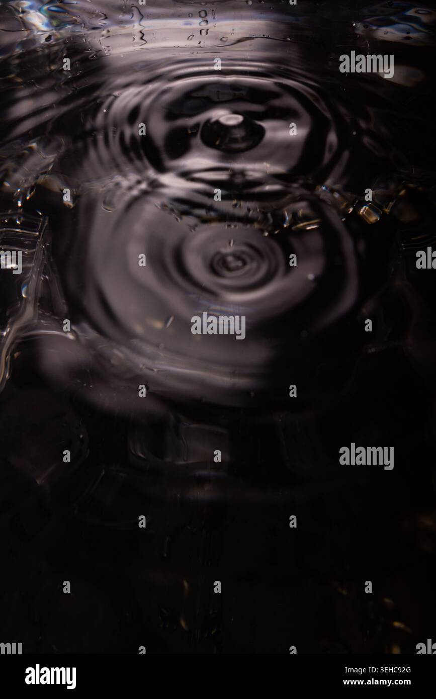 454.Close-up of water surface showing concentric ripple rings from central impact. High-contrast lighting highlights wave symmetry and texture. Image Stock Photo