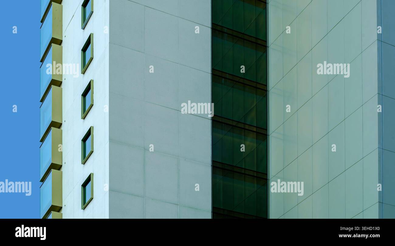 A vertical geometric detail of a contemporary building exterior featuring glass windows and white architectural panels under clear daylight Stock Photo