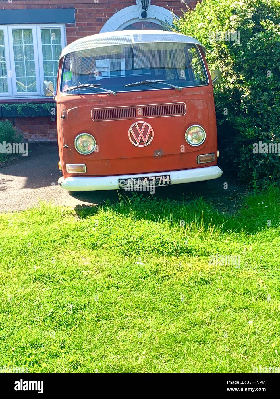 classic orange Volkswagen camper van parked outside a British home evoking retro road trip charm and timeless design in Northampton England - Smartphone Captured Stock Image