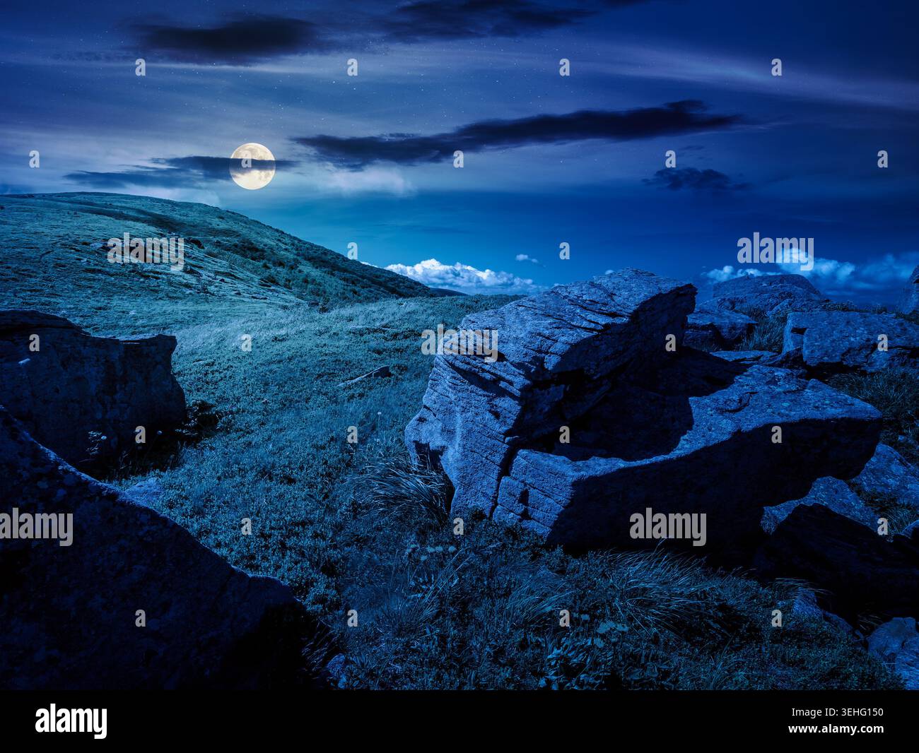 Carpathian mountain summer landscape at night. full moon over meadow with huge stones among the grass on top of the hillside near the peak of mountain Stock Photo