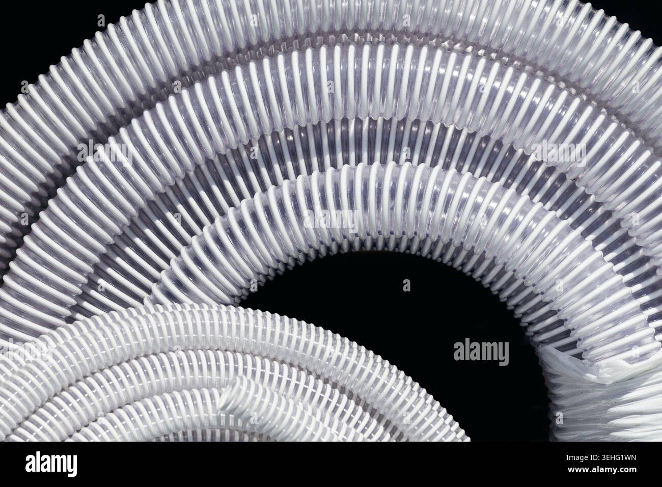 White corrugated plastic pipes neatly coiled against a solid black background. Selective focus. Stock Photo