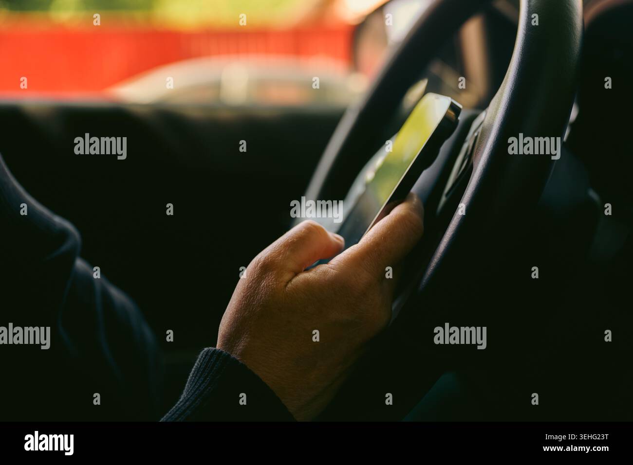 Driver using smartphone while holding steering wheel inside car, distracted driving concept, selective focus Stock Photo