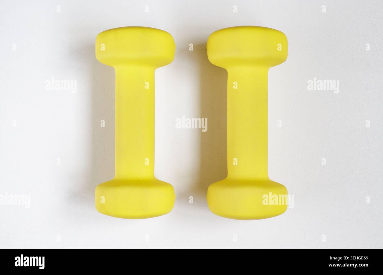 Small yellow dumbbells on a light gray background, preparation for home workouts. Kettlebells, corner, fitness, minimalist, sunny, floor, reusable. Sp Stock Photo