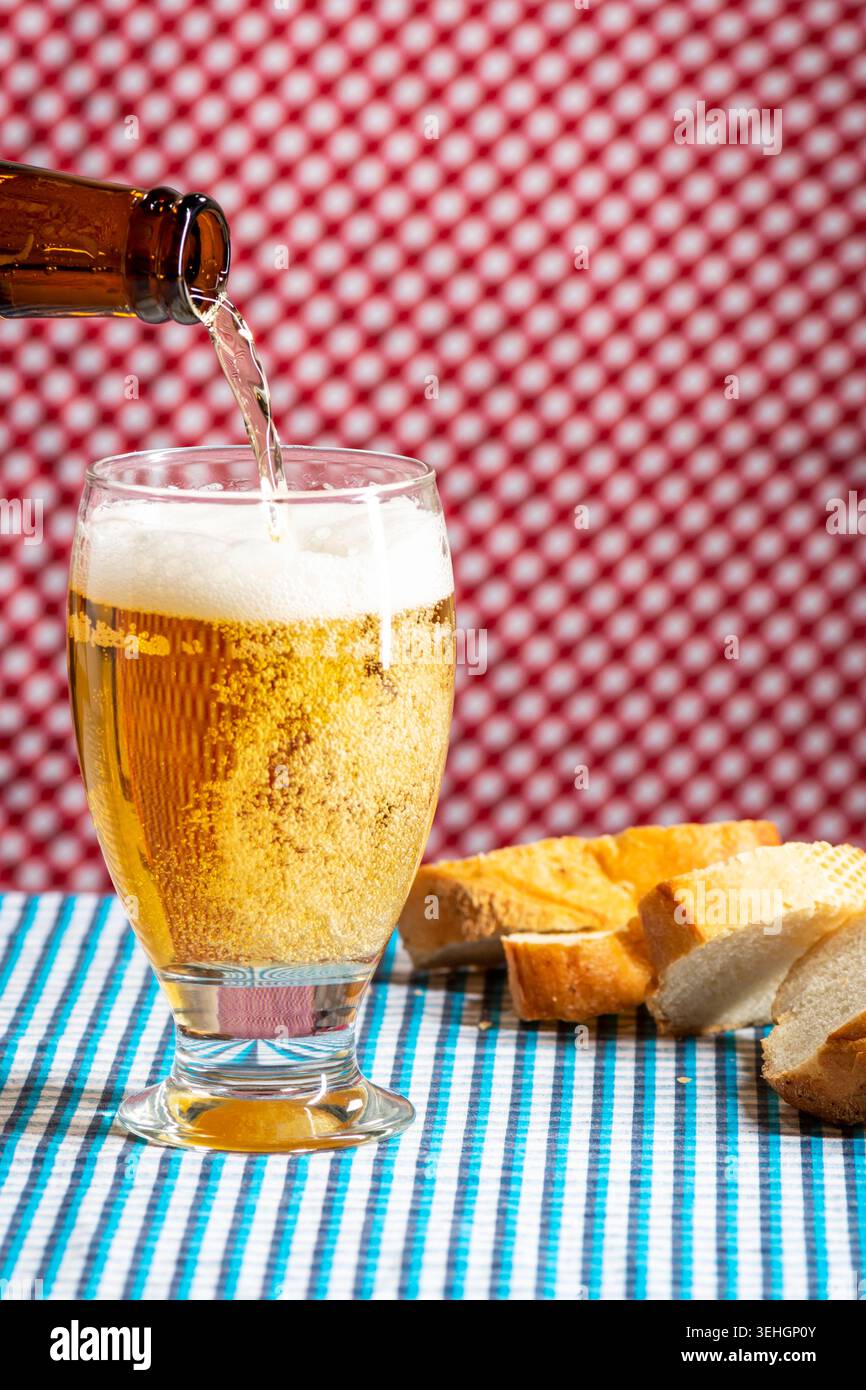Rustic Oktoberfest inspired scene with fresh beer being poured from a bottle into a glass beside sliced bread on a Bavarian table. Stock Photo