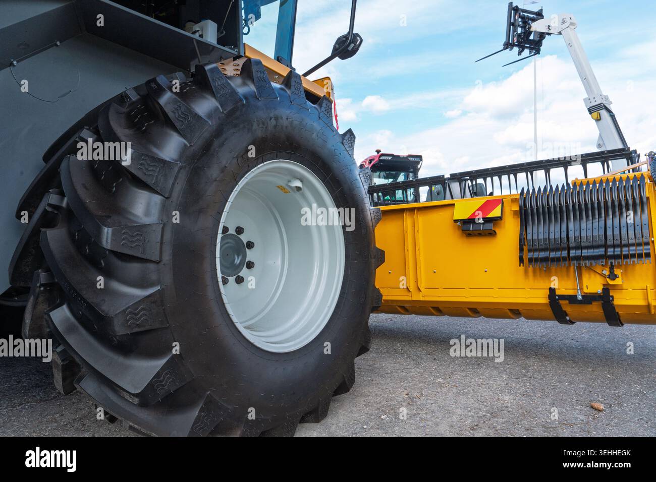 Close-up of a tractor tire and yellow agricultural machinery on display at a trade show Stock Photo