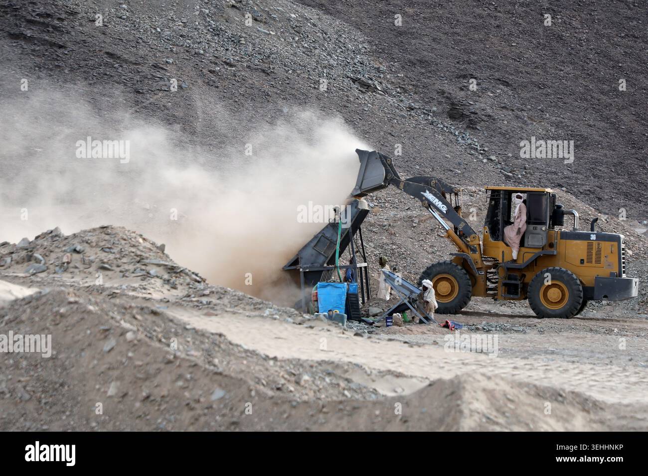 A front-loader deposits dirt and crushed rock into a processing machine ...