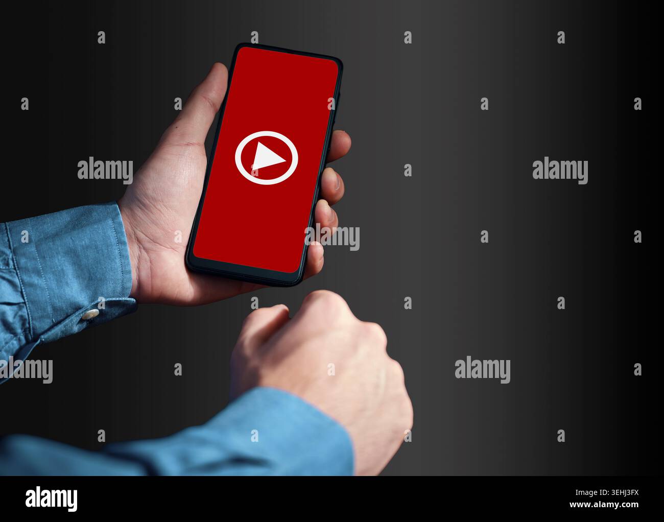 Person holding a smartphone, the screen displaying a red background with a white play button, indicating video content or streaming Stock Photo