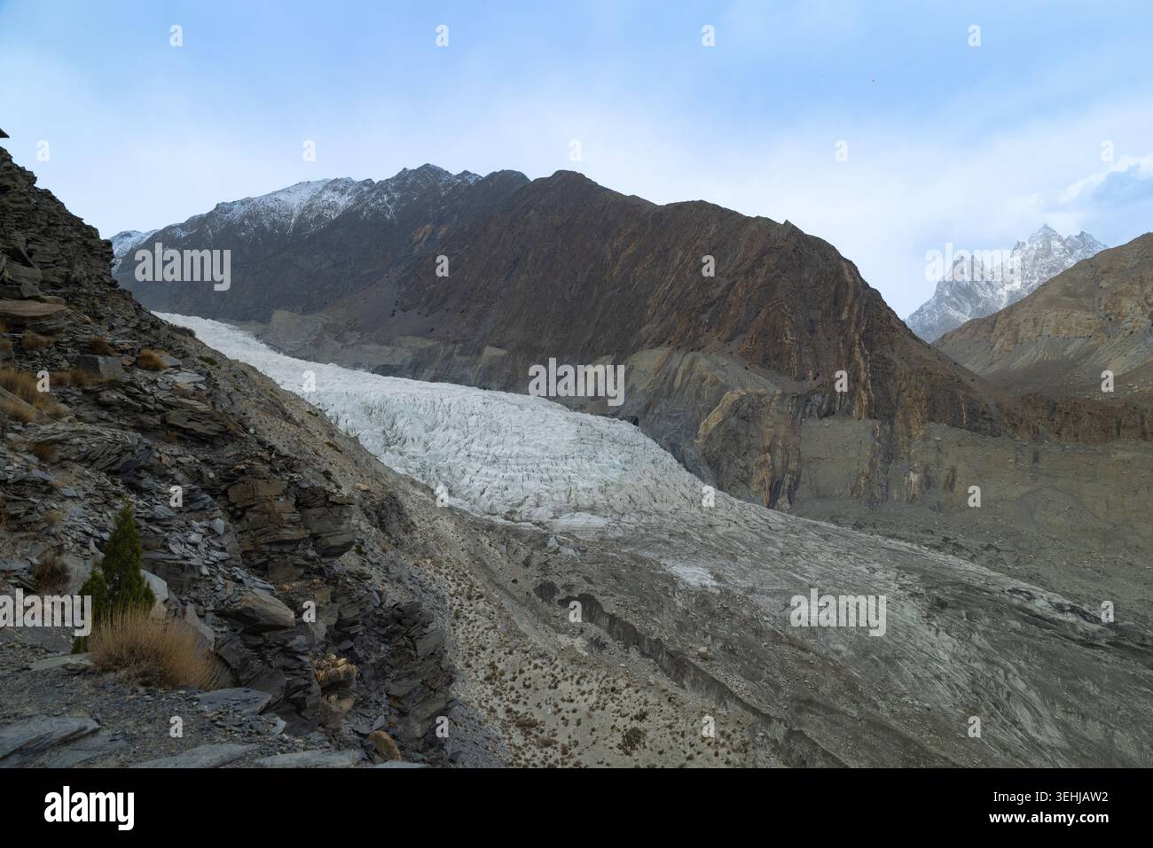View of a massive white glacier flowing between rugged mountain peaks under a cloudy sky Gilgit-Baltistan, Pakistan. Stock Photo