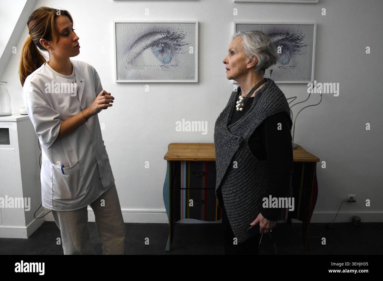An ocularist stands and talks to an older woman in a grey vest, in a ...