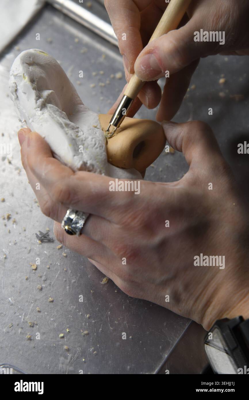 Ocularist using a small tool to sculpt a beige prosthetic eye, held in ...